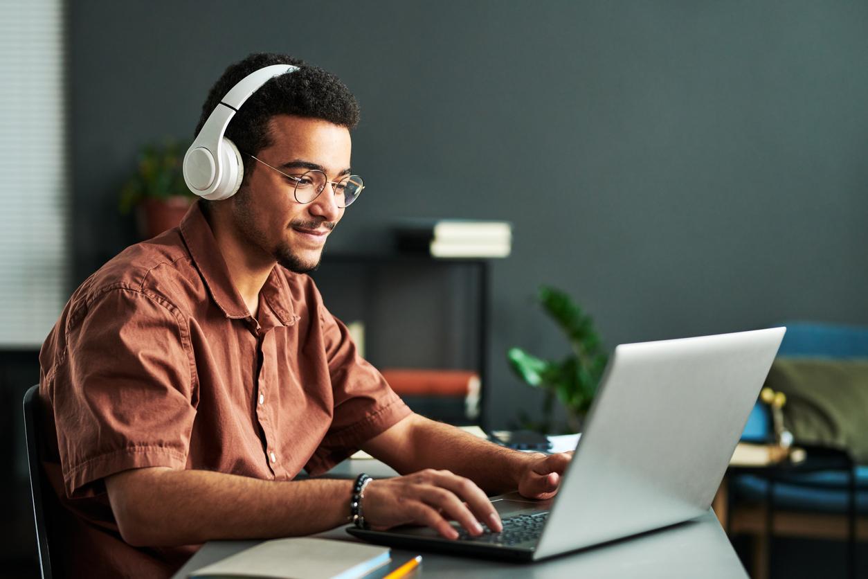 Man in his early 20s listening to music while sat at his laptop